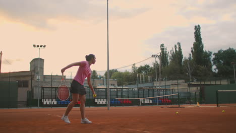 Slow-motion-of-woman-making-tennis-serve.-Slow-motion:-section-of-woman-bouncing-ball-on-tennis-court.-athlete-serves-the-tennis-ball.-Young-woman-is-hitting-the-ball-with-her-tennis-racket-at-sunset